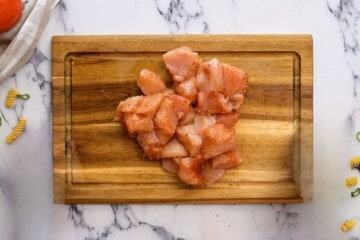 Cubed chicken seasoned with cajun seasoning on cutting board.