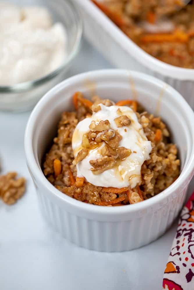 Bowl with carrot cake oatmeal topped with yogurt, walnuts, and maple syrup.