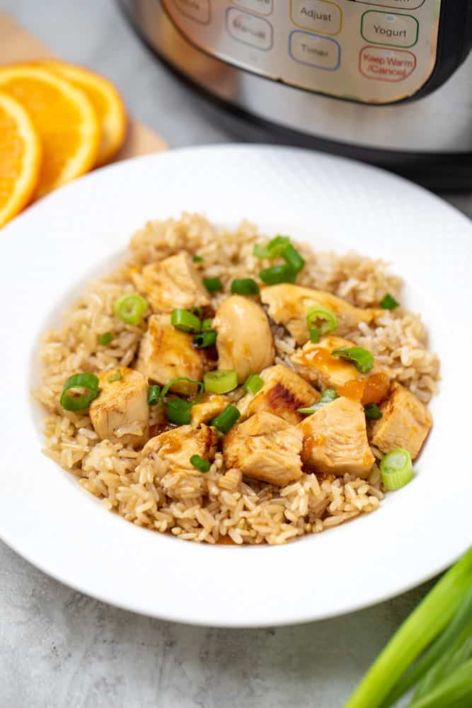 Bowl of orange chicken served over brown rice next to instant pot. 