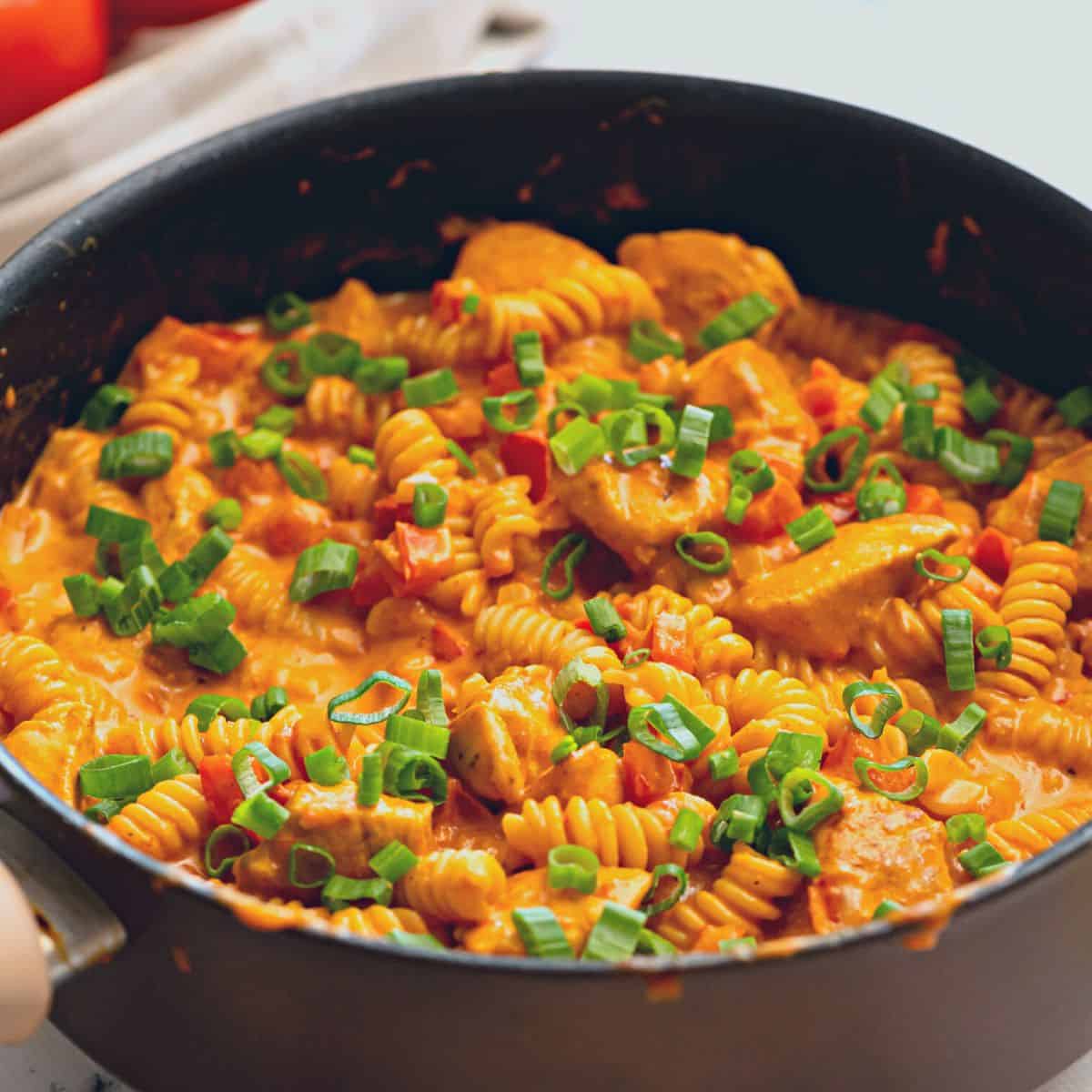 Skillet with Creamy Chicken Cajun Pasta topped with green onions.