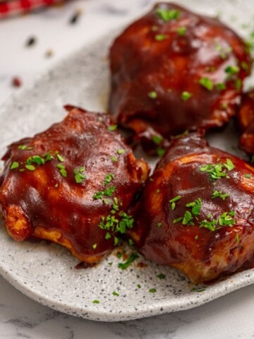 Close up of BBQ Chicken Thighs on white platter.
