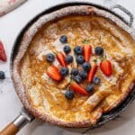 Fluffy crispy German pancake in skillet topped with berries.