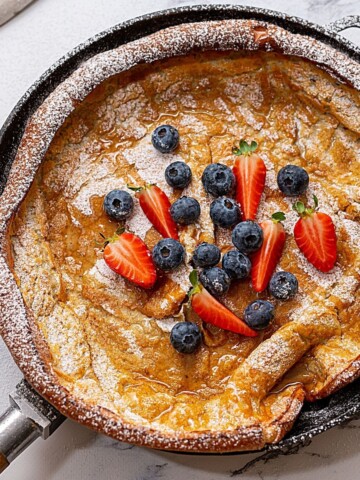 Fluffy crispy German pancake in skillet topped with berries.