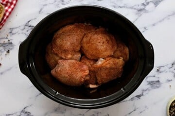 Seasoned raw chicken thighs in crockpot.