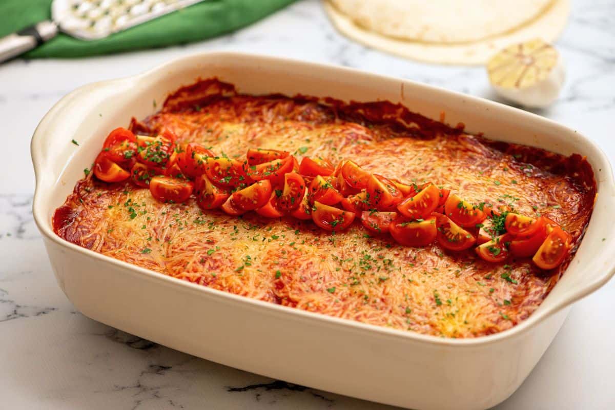 Baked Chicken enchilada casserole in baking dish topped with minced cilantro and diced tomatoes.