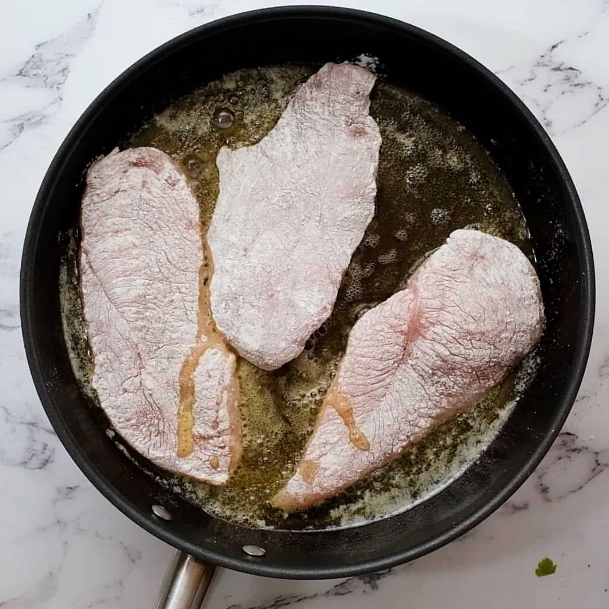 Chicken coated in flour in saute pan.
