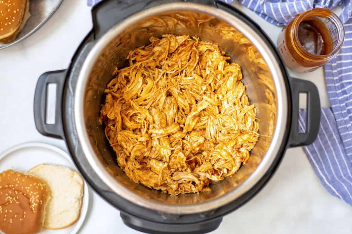 Shredded BBQ Chicken inside Instant Pot. Next to buns and bbq sauce.