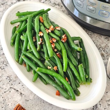Steamed green beans on white platter topped with pecans next to Instant Pot.