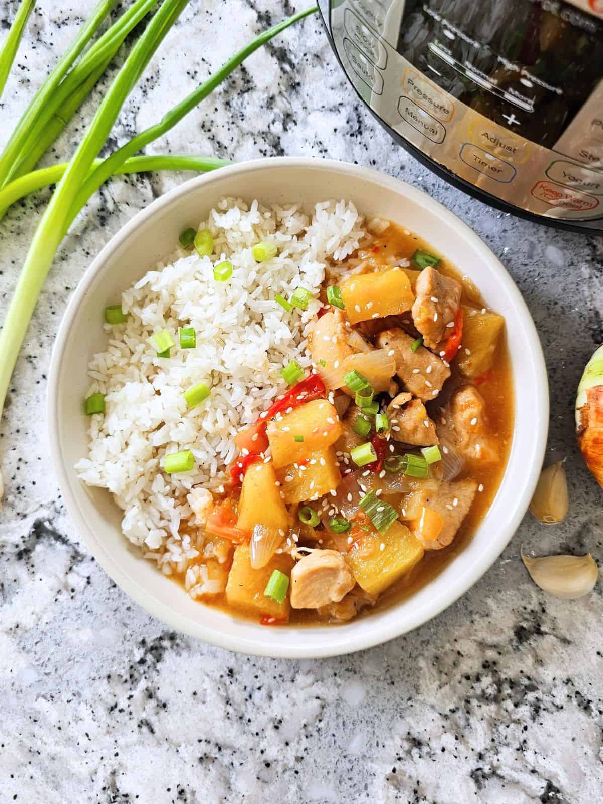 Sweet and sour chicken served next to rice with instant pot in background with green onions as well.