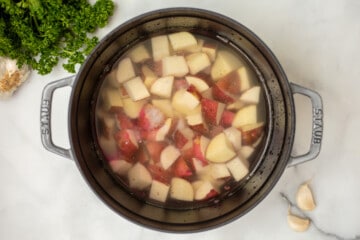 Red potato cubes in heavy-bottomed dish submerged in water.