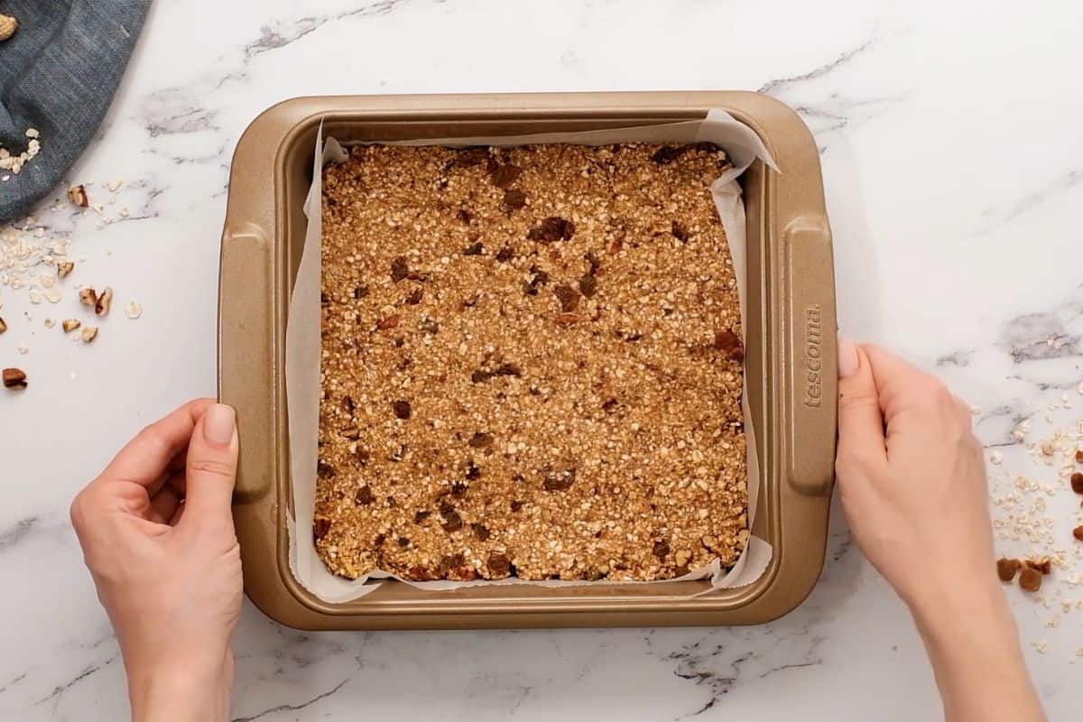 Granola bar mixture pressed into a baking dish that has been lined with parchment paper.