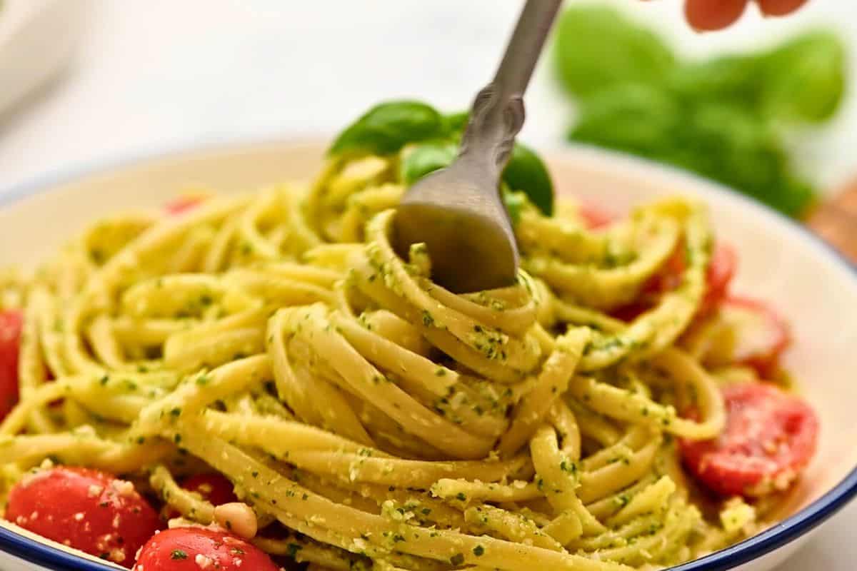 Fork swirling pasta noodles coated in pesto sauce.