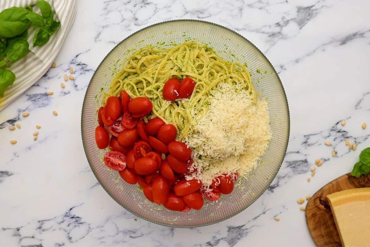 Large mixing bowl with cooked pasta, pesto, tomatoes, and parmesan.