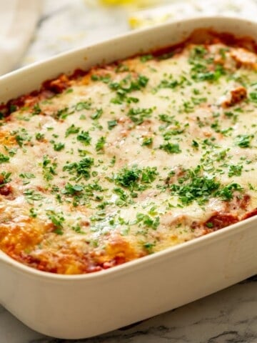 Baked Cheesy Ravioli with meat sauce in casserole dish topped with parsley.