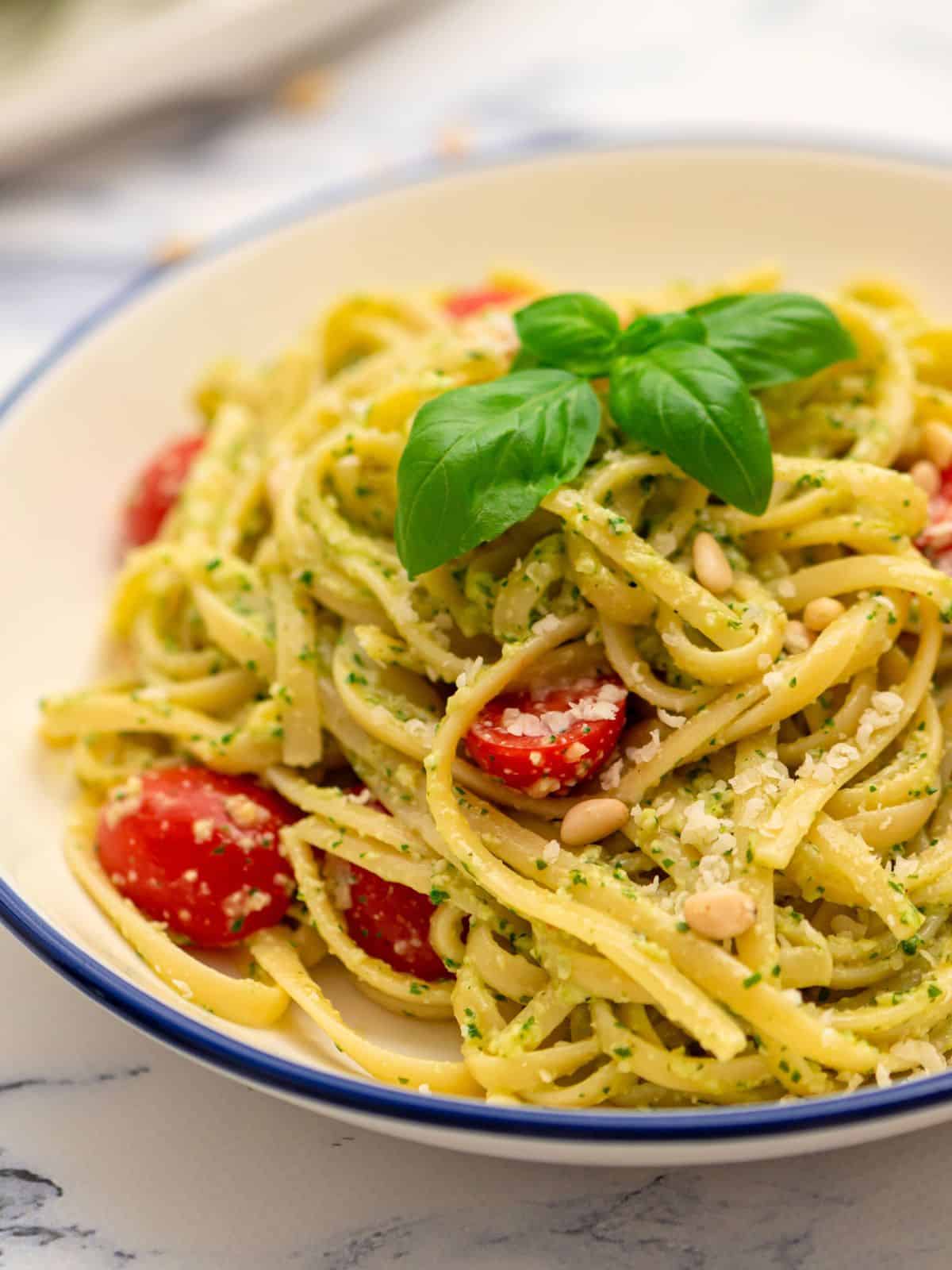Bowl of pesto pasta tossed with fresh tomatoes and basil.