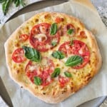 Baked tomato pizza topped with freshly grated parmesan cheese and fresh basil leaves on pizza pan topped with parchment paper.