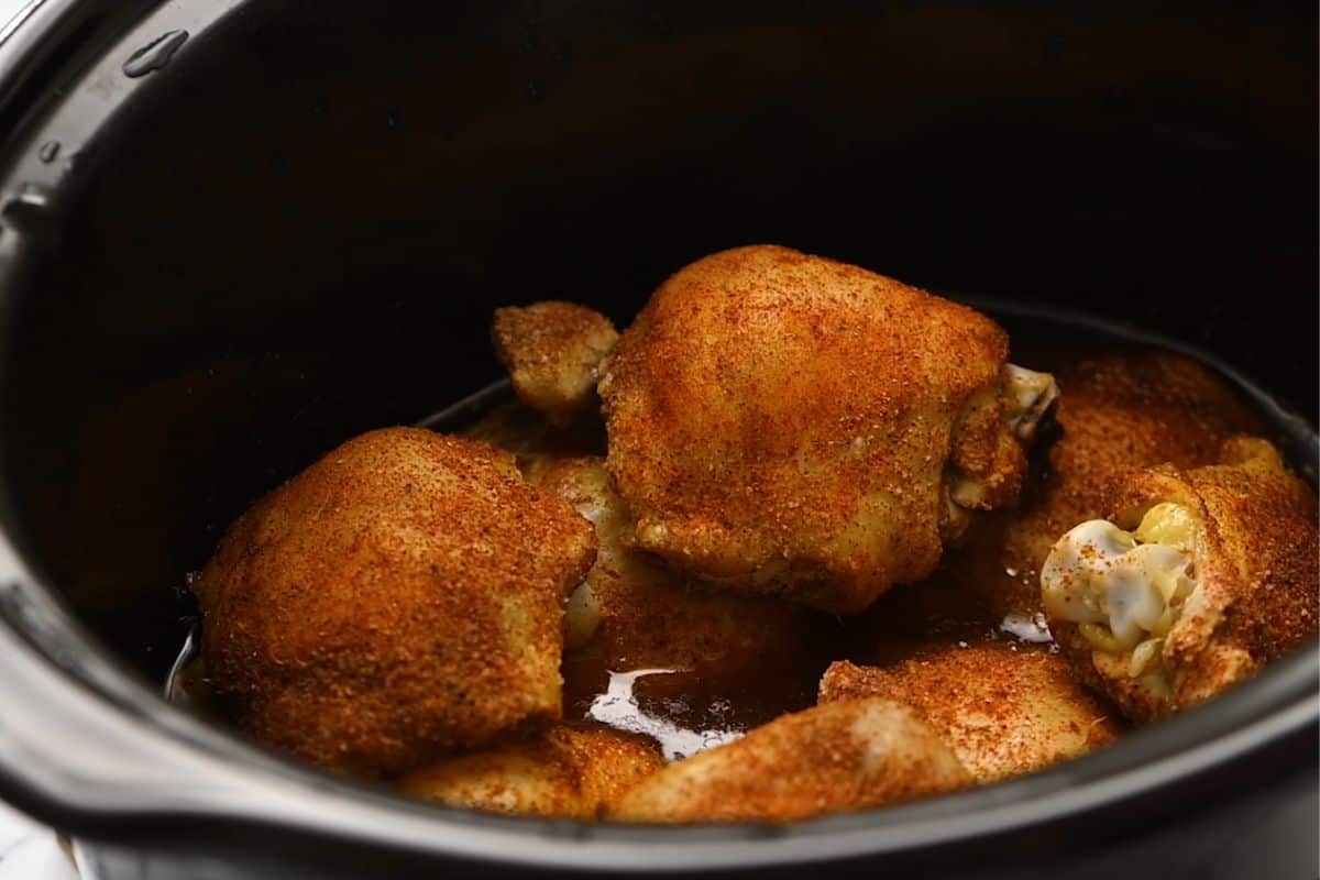 Cooked seasoned chicken thighs in the slow cooker.