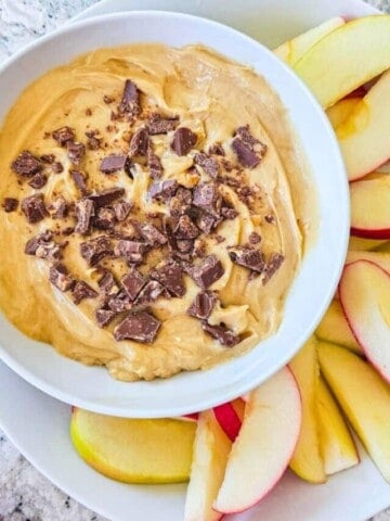 Cream Cheese Apple Dip in white dish topped with chopped toffee bar and served with sliced apples on the side.