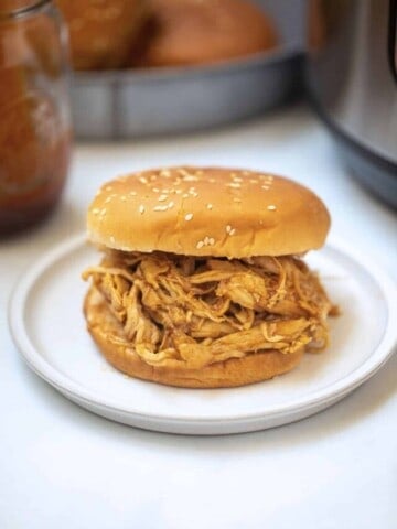 Shredded Instant Pot BBQ Chicken on bun with instant pot in background.