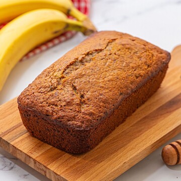 Loaf of banana bread on wooden cutting board.