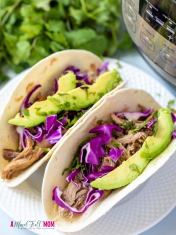 2 pork tacos on a white plate topped with cabbage and avocado