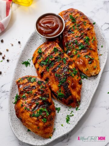 Grilled BBQ Chicken on white platter topped with parsley.