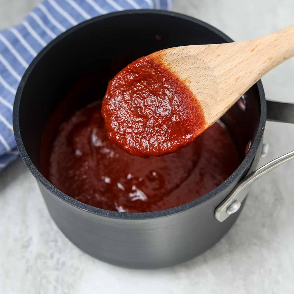 Wooden spoon stirring barbecue sauce in stock pan.