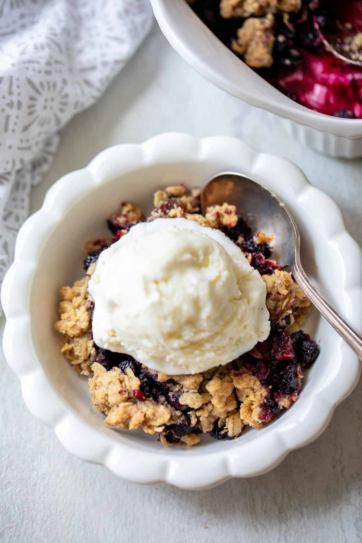 Berry Crisp dished out in white bowl and topped with vanilla ice cream.