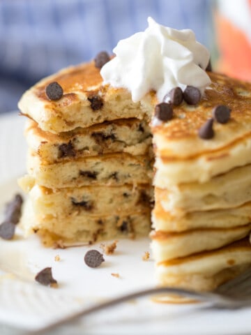 Stack of chocolate chip pancakes with bite taken out of center revealing chocolate chips.