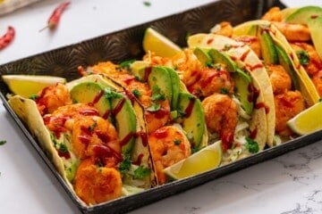 Shrimp tacos on serving platter drizzled with hot sauce.