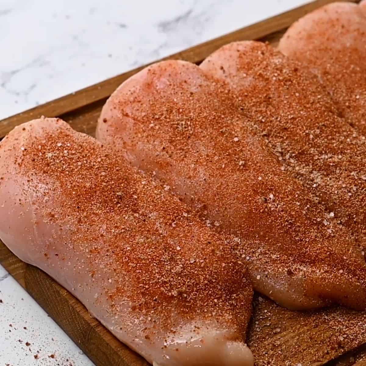 Raw chicken breasts with dry rub over chicken.