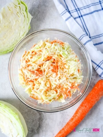 Bowl of homemade coleslaw next to carrots and cabbage.