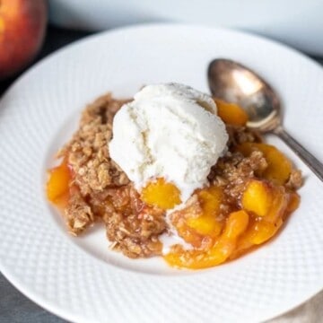 Peach Crisp on white plate topped with ice cream.