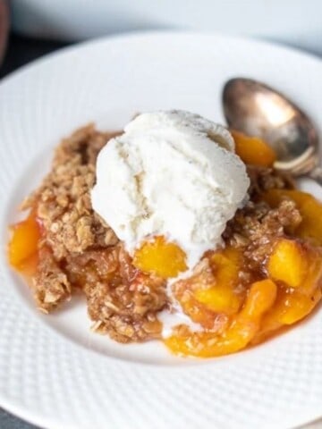 Peach Crisp on white plate topped with ice cream.