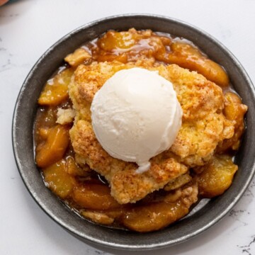 Peach Cobbler topped with vanilla ice cream on silver plate.