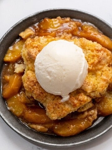 Peach Cobbler topped with vanilla ice cream on silver plate.