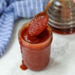 Spoon scooping out BBQ sauce from glass jar.