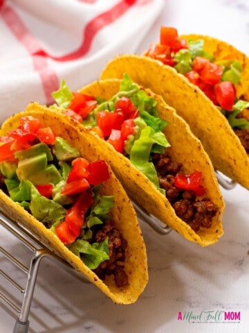 3 hard shell tacos with beef, lettuce, and tomatoes.