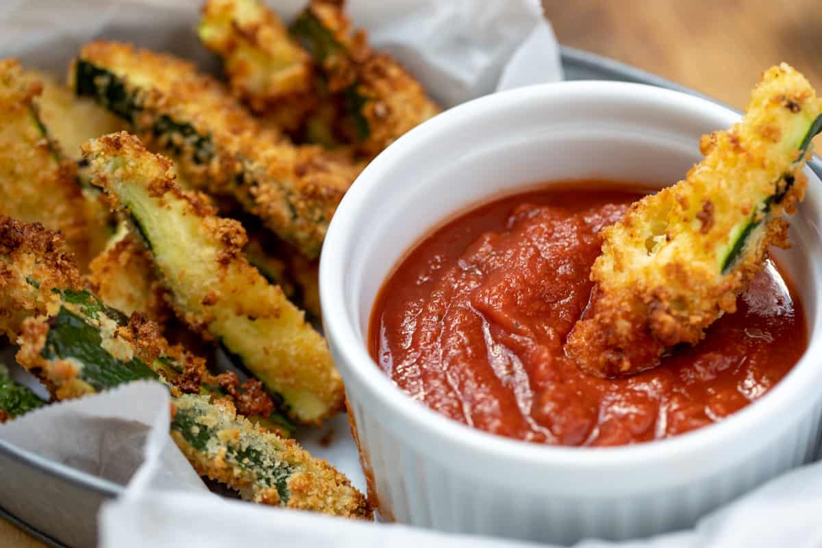 Parmesan Zucchini Fries in a basket with one dipping into marinara sauce. 