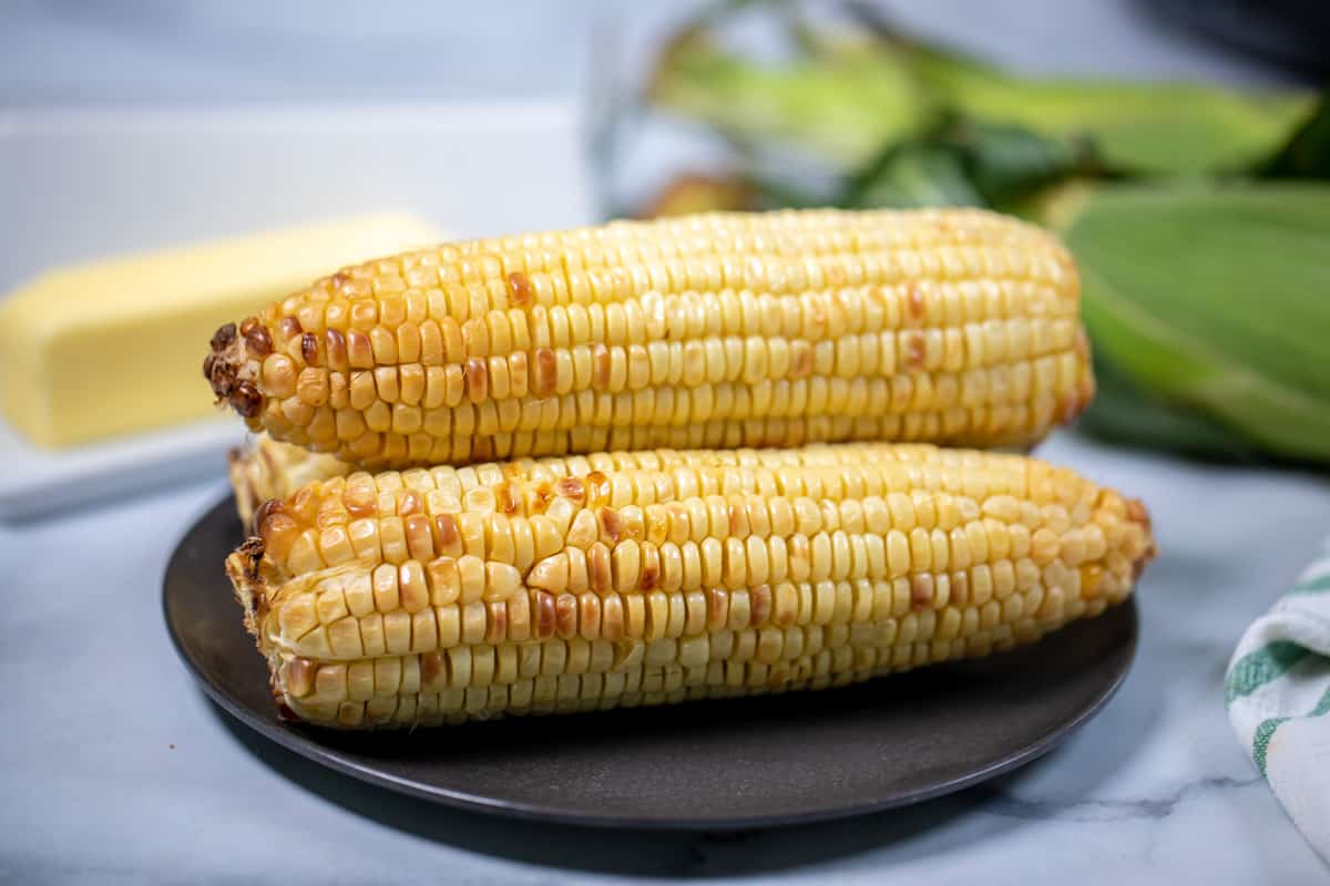 3 ears of air fried corn on a black plate.