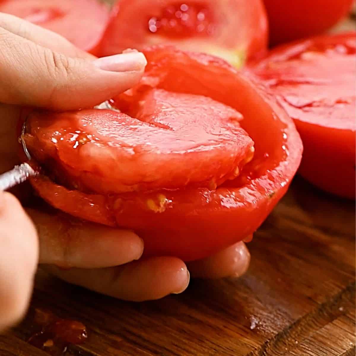 Using a spoon to scoop out the seeds of the tomatoes. 