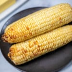 3 ears of air fried corn on a black plate.