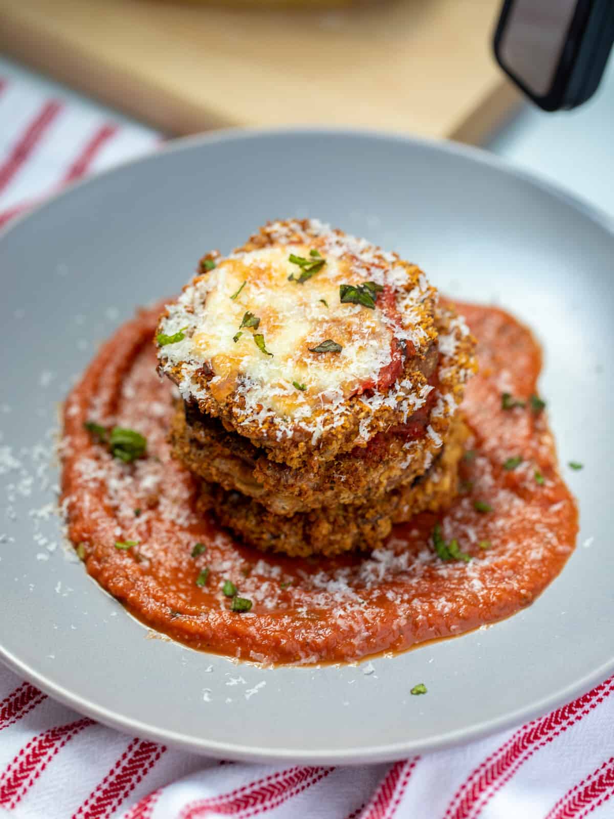 Stack of air fryer eggplant parmesan on gray plate topped with parmesan. 