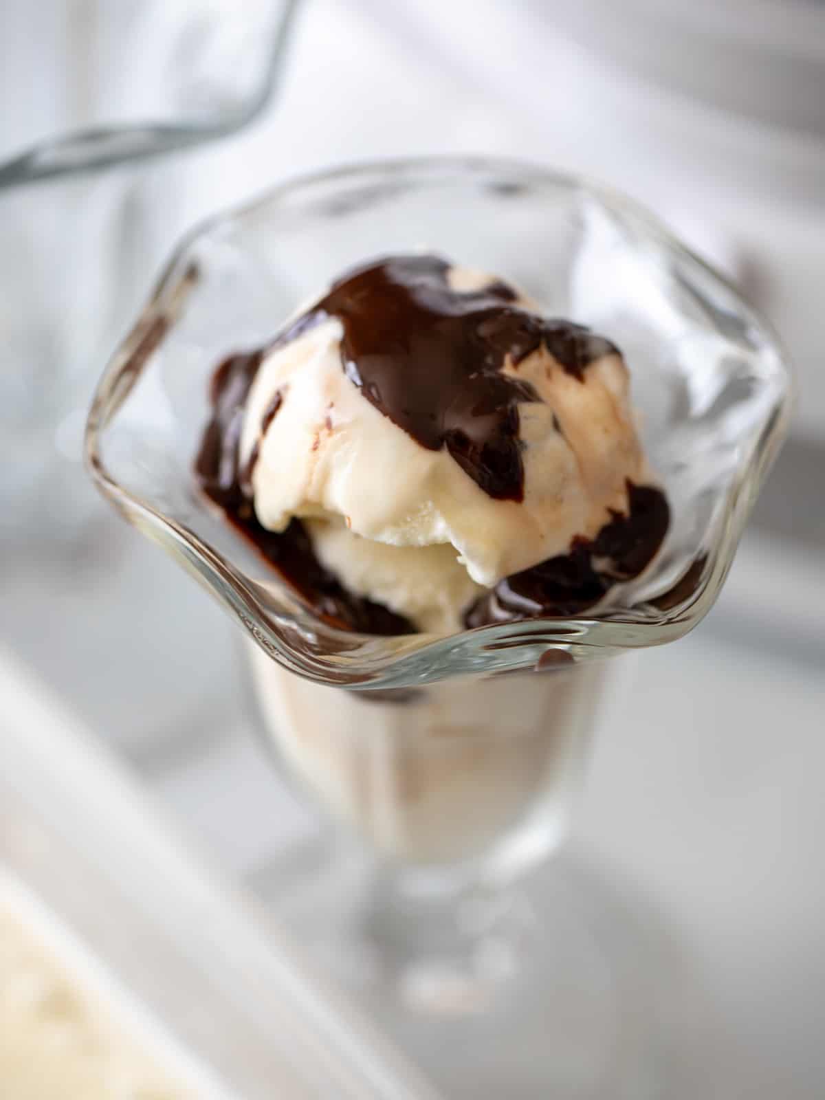 Homemade vanilla ice cream in sundae bowl topped with hot fudge. 