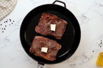 Ribeye steaks in skillet after searing with butter.