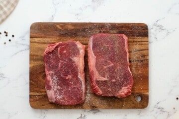 Two Seasoned Ribeye Steaks on cutting board.