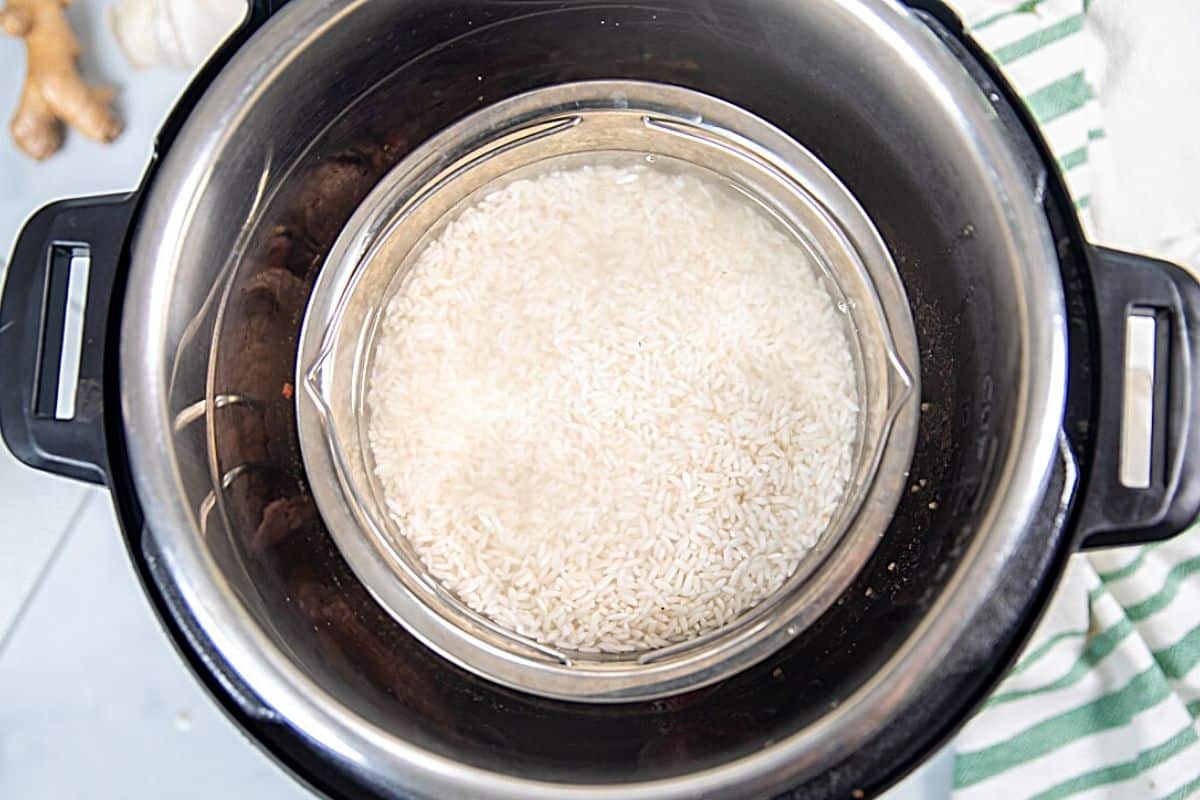 Stainless steel bowl of white rice on rack in inner pot of instant pot. 