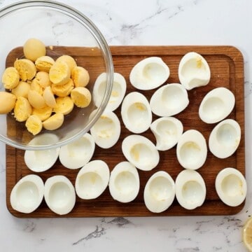 Hard boiled eggs cut in half with whites on cutting board and yolks in mixing bowl.