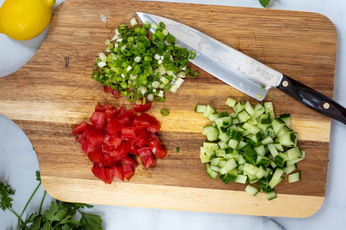 Cucumbers, tomatoes, and green onions on wooden cutting board. 