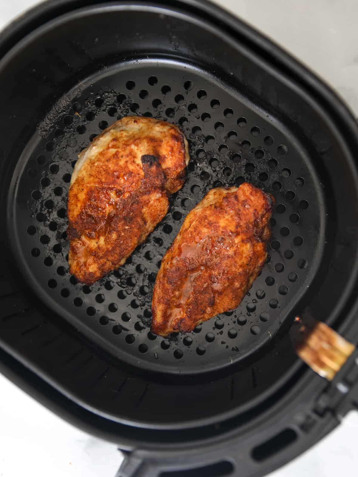 2 golden brown spice-rubbed chicken breasts in air fryer. 